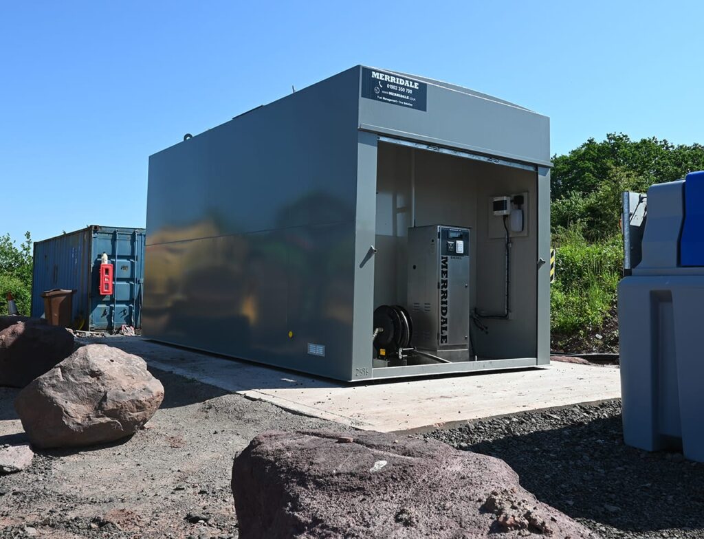 An outdoor shot of a grey Merridale commercial fuel storage tank with a built-in dispensing cabinet containing a stainless steel diesel pump and hose reel system, positioned on a concrete base at an industrial site.